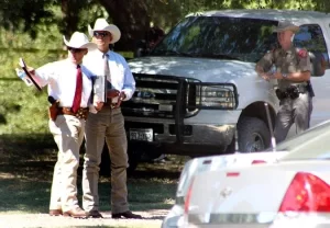 Two Texas Rangers talking while a State trooper looks on, leaning against a white pickup truck.