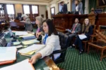 Secretary of the Senate and staff seated in front of the dais in the Texas Senate Chamber.
