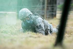 Soldier wearing gas mask lying on ground crawling through barbed wire