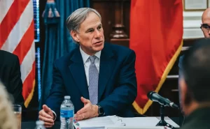 Governor Greg Abbott seated next to Speaker Dennis Bonnen with U.S. and texas flags behind him.