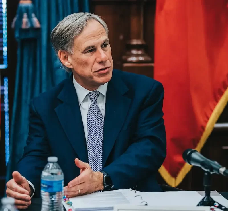 Governor Greg Abbott seated next to Speaker Dennis Bonnen with U.S. and texas flags behind him.