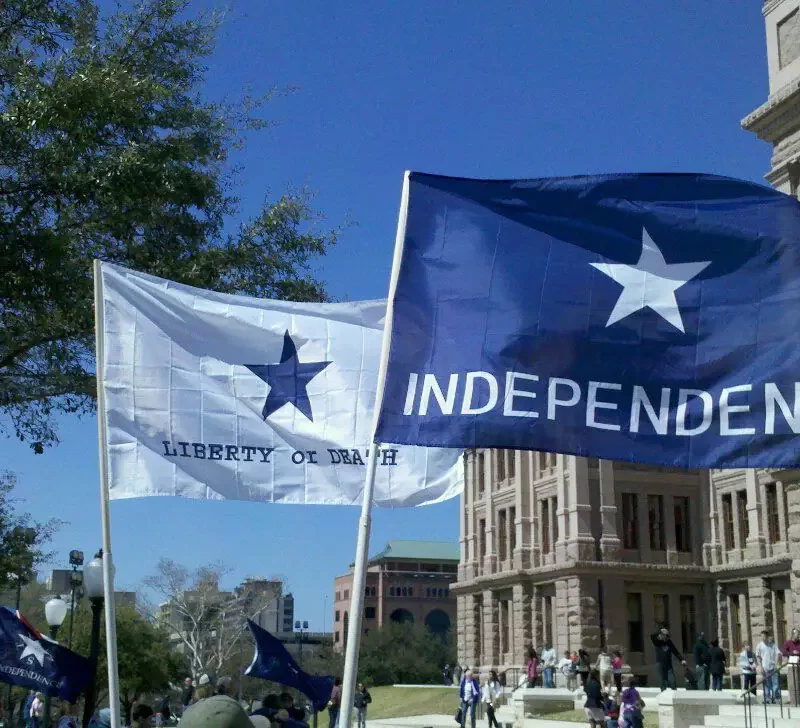 Flags of the Texas Nationalist Movement (TNM), a separatist organization, saying "Independence" and "LIberty or Death," flying in front of the Texas Capitol during a demonstration by secessionists.