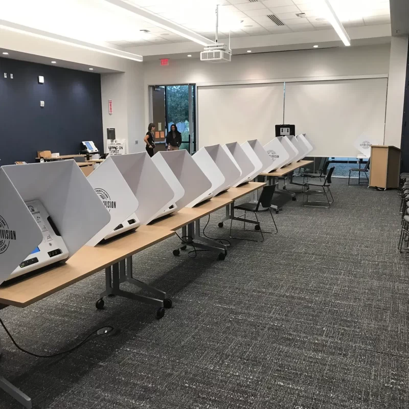 Row of voting machines in Texas with election officials in background.