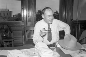 Texas Governor Coke Stevenson sitting at his desk with a pipe.