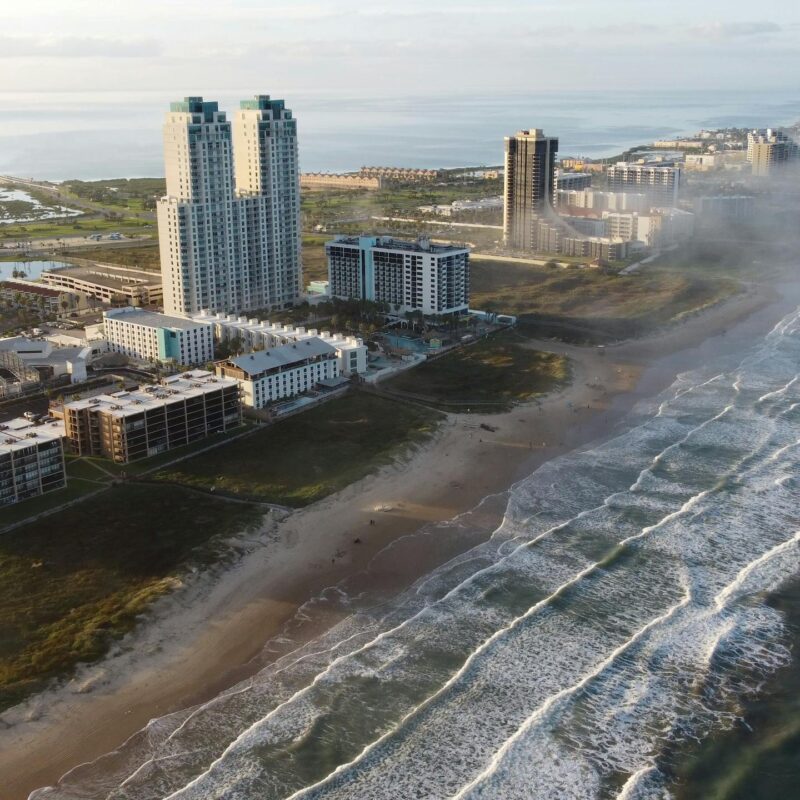 Sunrise aerial of South Padre Island's coastline with tall buildings and waves.